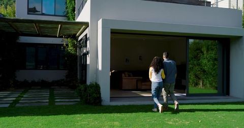 Couple Walking Across Lawn Toward Modern Home’s Sliding Glass Door
