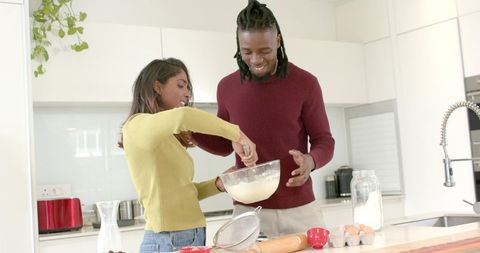 Diverse couple baking together mixing batter on modern sunlit kitchen island