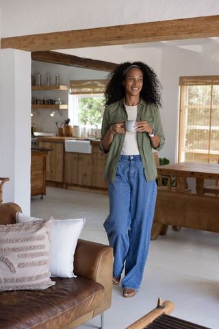 Woman holding coffee mug walking through cozy rustic open-plan kitchen and living area