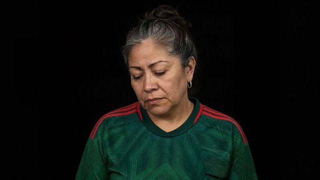 Contemplative midlife woman wearing green soccer jersey looking down on black backdrop