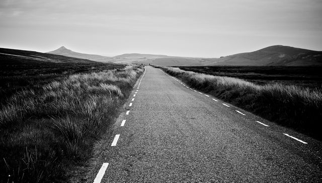 Deserted road stretching into horizon in black and white conveys a sense of solitude and journey. Ideal for use in travel-themed promotions, adventure or journey narratives, and artistic prints highlighting isolation and tranquility.