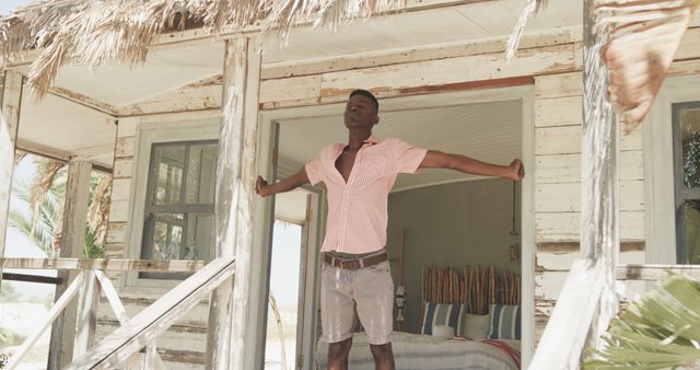 African american man stretching outside house on beach. Lifestyle, nature, relaxation, vacation, summer and leisure, unaltered.