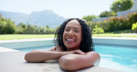 African american woman smiling, relaxing in backyard pool with sunglasses, mountain view