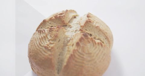 Rustic round artisan loaf resting on white surface with scored cross and banneton ridges