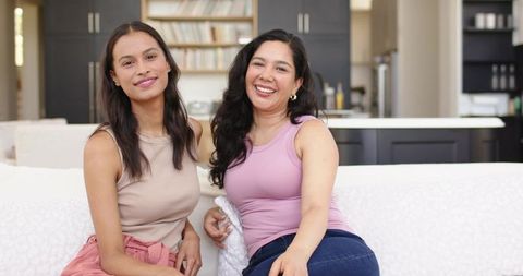 Two friends relaxing and smiling on white sofa in modern open-plan kitchen interior