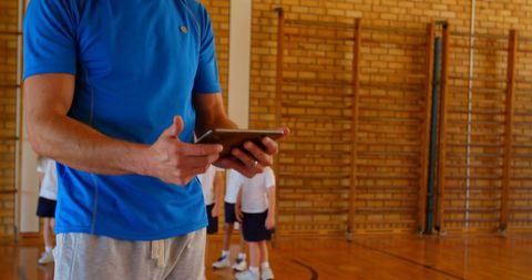 Sports Coach Observing Students with Digital Tablet in Basketball Gym