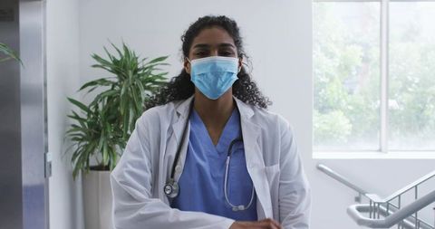 Confident female doctor wearing surgical mask and stethoscope standing in clinic corridor