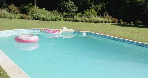 Colorful donut and popsicle floats drifting on backyard pool with garden reflection