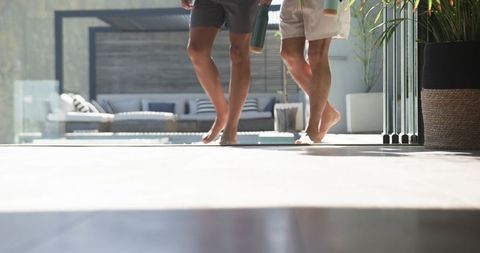 Two men walking barefoot across poolside patio carrying reusable tumblers sunlit terrace