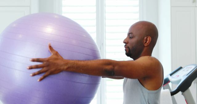 Man using a stability ball for a fitness workout in a home gym environment. This image is suitable for illustrating home fitness routines, exercise guides, personal training programs, and health-related websites.