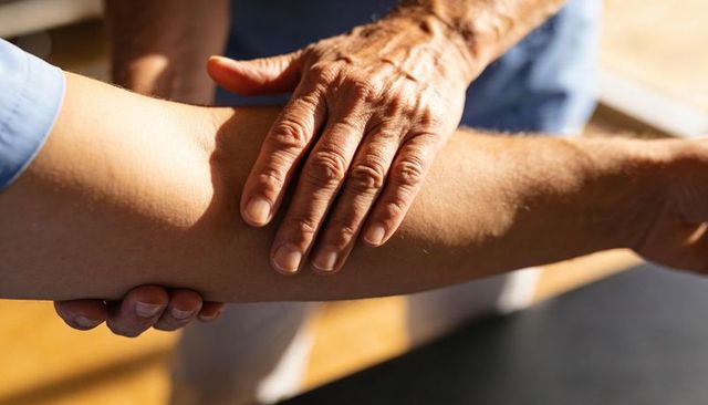 Therapist palpating forearm under warm sunlight closeup showing caring manual assessment