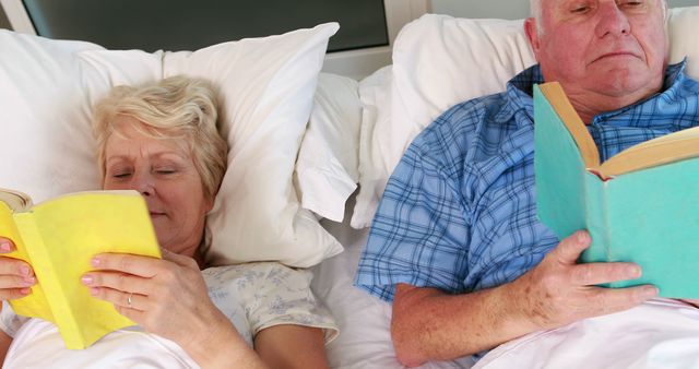 This image shows an older couple comfortably lying in bed while reading books. It highlights relaxation and the joy of reading, portraying the peaceful and loving moments shared by the elderly. This can be used for themes of retirement, aging, hobbies, companionship, and wellness for older adults.