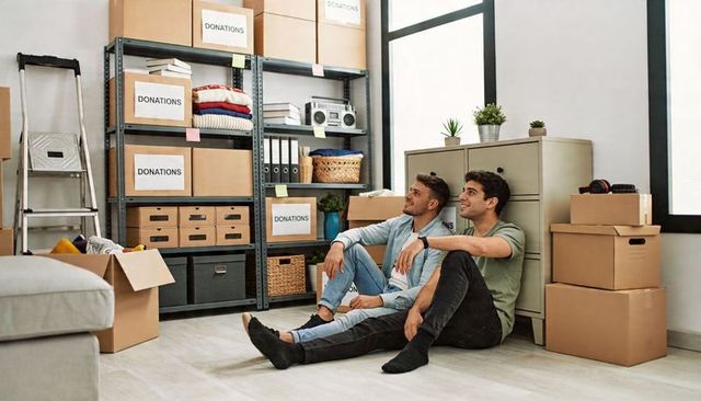Two young men sitting among labeled donation boxes organizing charity storage space