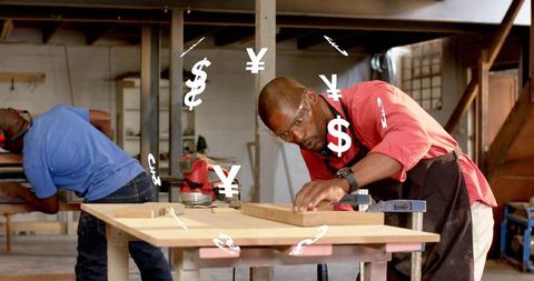 Skilled woodworker marking clamped board on workbench wearing safety goggles and apron