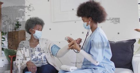 Home nurse measuring blood pressure of elderly patient wearing mask during care visit