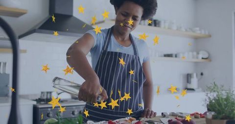 Home cook drizzling olive oil onto chopped vegetables on board in kitchen with gold stars