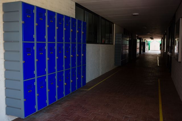 Blue lockers line the wall of a school corridor, providing storage for students. The hallway is empty, suggesting a quiet moment during class time or after school hours. This image can be used for educational content, school brochures, articles on student life, or organizational tools in academic settings.