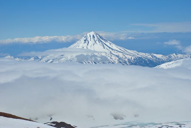 The snow-capped peak of a mountain rises majestically above a sea of clouds. This natural scene can be used in travel brochures, nature magazines, scenic calendars, and adventure tourism promotions to invoke a sense of awe, tranquility, and pristine beauty.