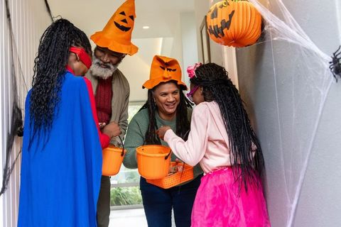 African american family handing out halloween candy at decorated porch with pumpkin hats