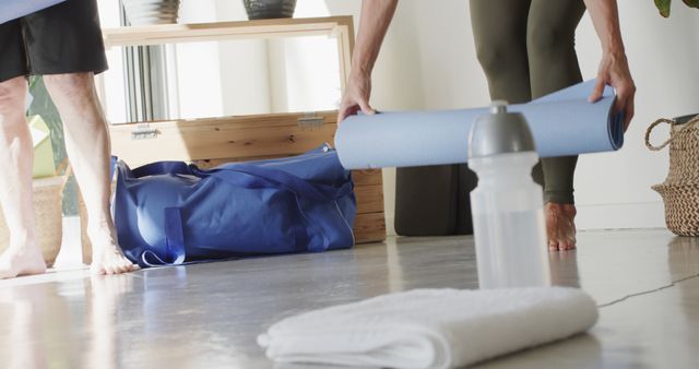Individuals preparing for an indoor fitness session, focusing on unrolling yoga mats. Ideal for illustrating healthy lifestyle, fitness routines, exercise preparation, and wellness themes in websites or blogs promoting fitness, health tips, or product advertisements for yoga equipment and accessories.