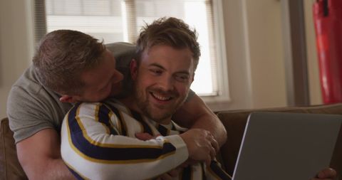 Happy Same-Sex Couple Embracing and Sharing Laptop Moment at Home