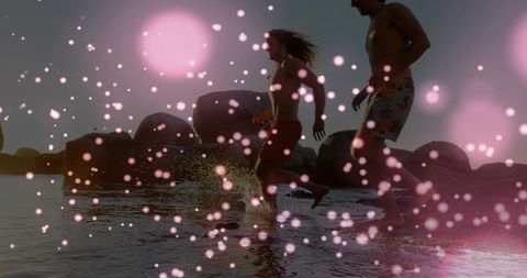 Sunset silhouette couple running on rocky shoreline with pink bokeh and splash