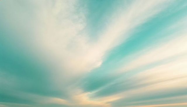 Radiating teal and peach sky streaks at sunrise over distant horizon pastel cirrus gradient