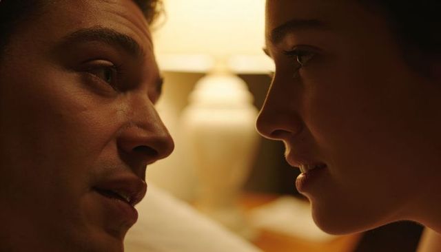 Couple whispering in warm bedside lamp light leaning close for intimate late-night moment