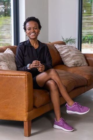 African american woman sitting on leather sofa smiling while wearing smartwatch and purple sneakers