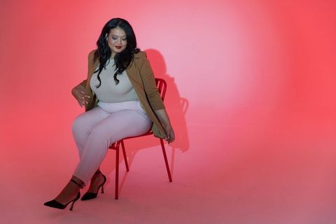Confident woman sitting on red chair adjusting blazer hem in minimalist fashion portrait