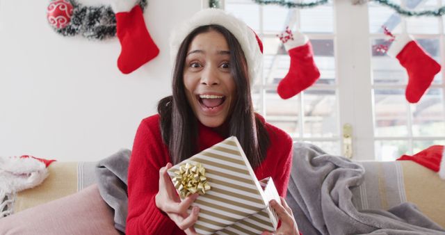 Excited Woman in Santa Hat Opening Christmas Present by Decorated Fireplace - Download Free Stock Images Pikwizard.com