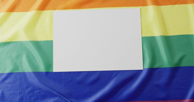 Blank white sign lying on rainbow LGBTQ flag, ideal for adding personalized messages about equality, diversity, or inclusion. Perfect for use in promotional materials, social media campaigns, and support messages during pride parades and LGBTQ events.