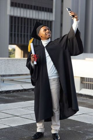 African American graduate taking selfie on urban rooftop holding diploma and yellow tassel