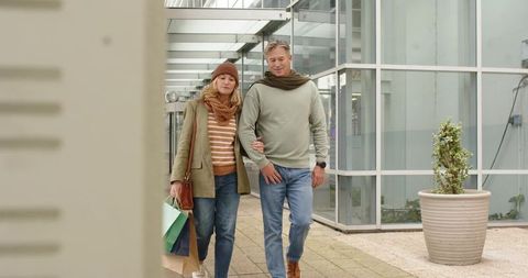 Mature couple walking through glass arcade carrying shopping bags casual fall fashion
