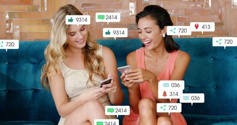 Young women laughing and scrolling phones on teal tufted sofa with social media alerts