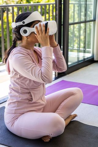 Woman wearing vr headset practicing mindful yoga on balcony in pale pink athleisure