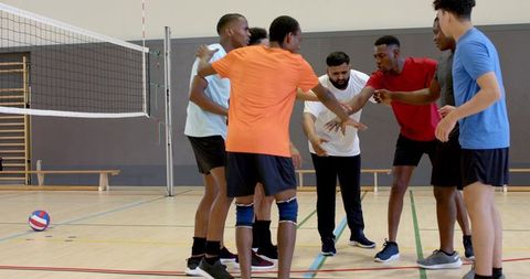 Diverse male volleyball team huddling on indoor court showing unity, strategy, teamwork
