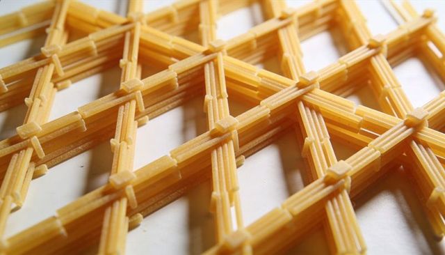 Short ribbed pasta sticks forming geometric lattice with square connectors casting shadows