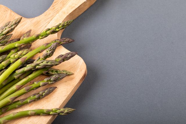 Fresh asparagus on a wooden cutting board over a gray background. Ideal for use in healthy eating and organic food promotions, recipe blogs, diet and nutrition articles, and culinary websites. The copy space allows for easy addition of text or branding.