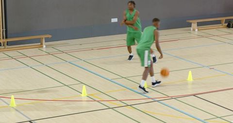 Diverse male players dribbling basketballs around cones during indoor agility drill