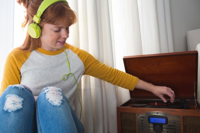 Young woman wearing headphones, sitting on floor, enjoying music from vintage gramophone. Ideal for use in lifestyle blogs, music-related content, retro-themed promotions, and home decor inspiration.