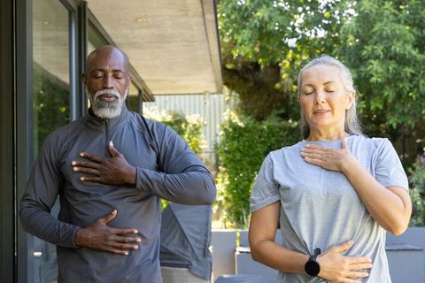 Mature interracial couple practicing paced breathing and mindfulness on sunlit patio for wellness