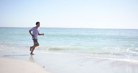 Young Man Jogging on Sunny Beachfront for Fitness