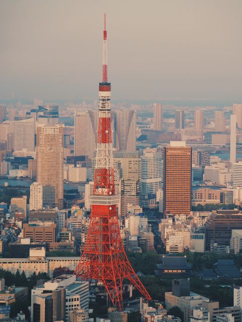 Tokyo Tower prominently rising amidst a dense urban landscape with buildings illuminated by the soft light of sunset. The famous orange and white structure is an iconic symbol of Tokyo, Japan. Ideal for travel websites, cultural presentations, urban development projects, and tourism brochures.