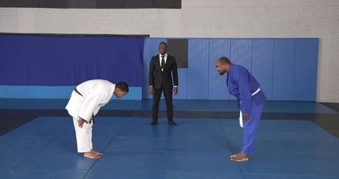 Martial Artists Bowing with Referee in Professional Gym