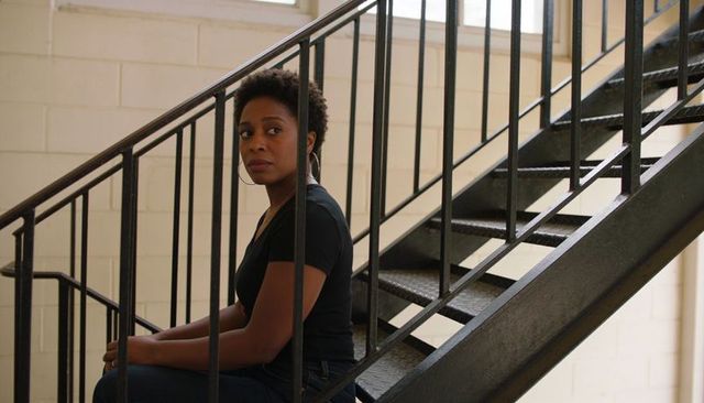Contemplative woman sitting on stairwell wearing black top, jeans and hoop earrings