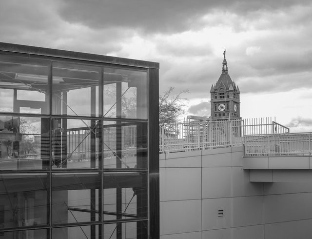 Depicts urban scene with sleek, modern architecture contrasted by historic clock tower in black and white; can be used for themes of urban development, architectural contrast, and history vs modernity. Suitable for articles on city evolution, urban planning, or architectural photography collections.