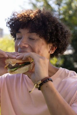 Young woman enjoying cheeseburger in sunlit park