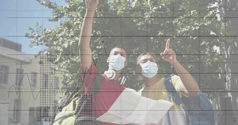 Masked young travelers holding map pointing on sunlit urban street navigating with backpacks