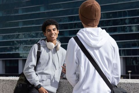 Two students chatting on campus terrace wearing hoodies and headphones, casual friendship